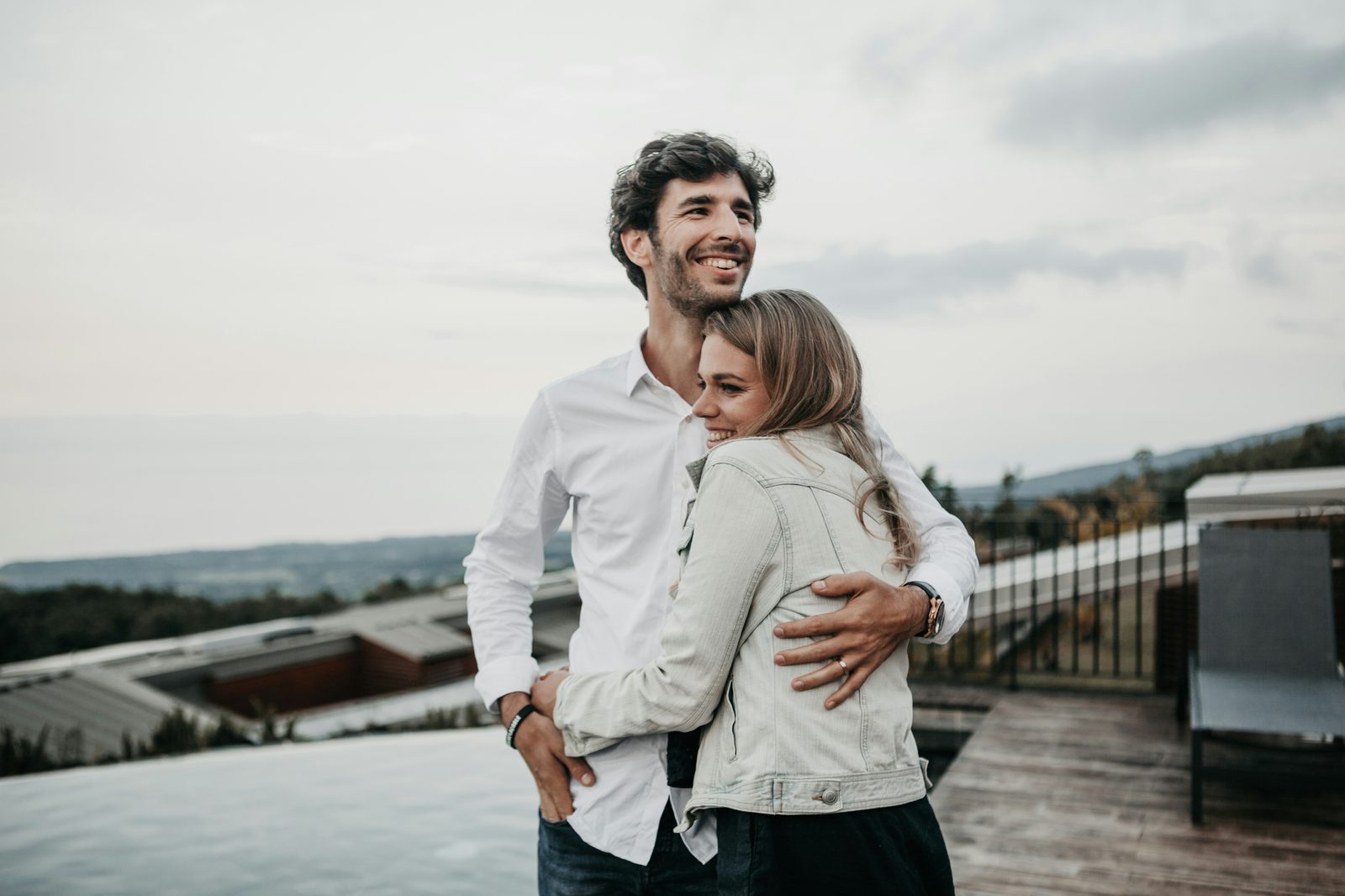 A man holding his partner close on a rooftop, both looking out at the view